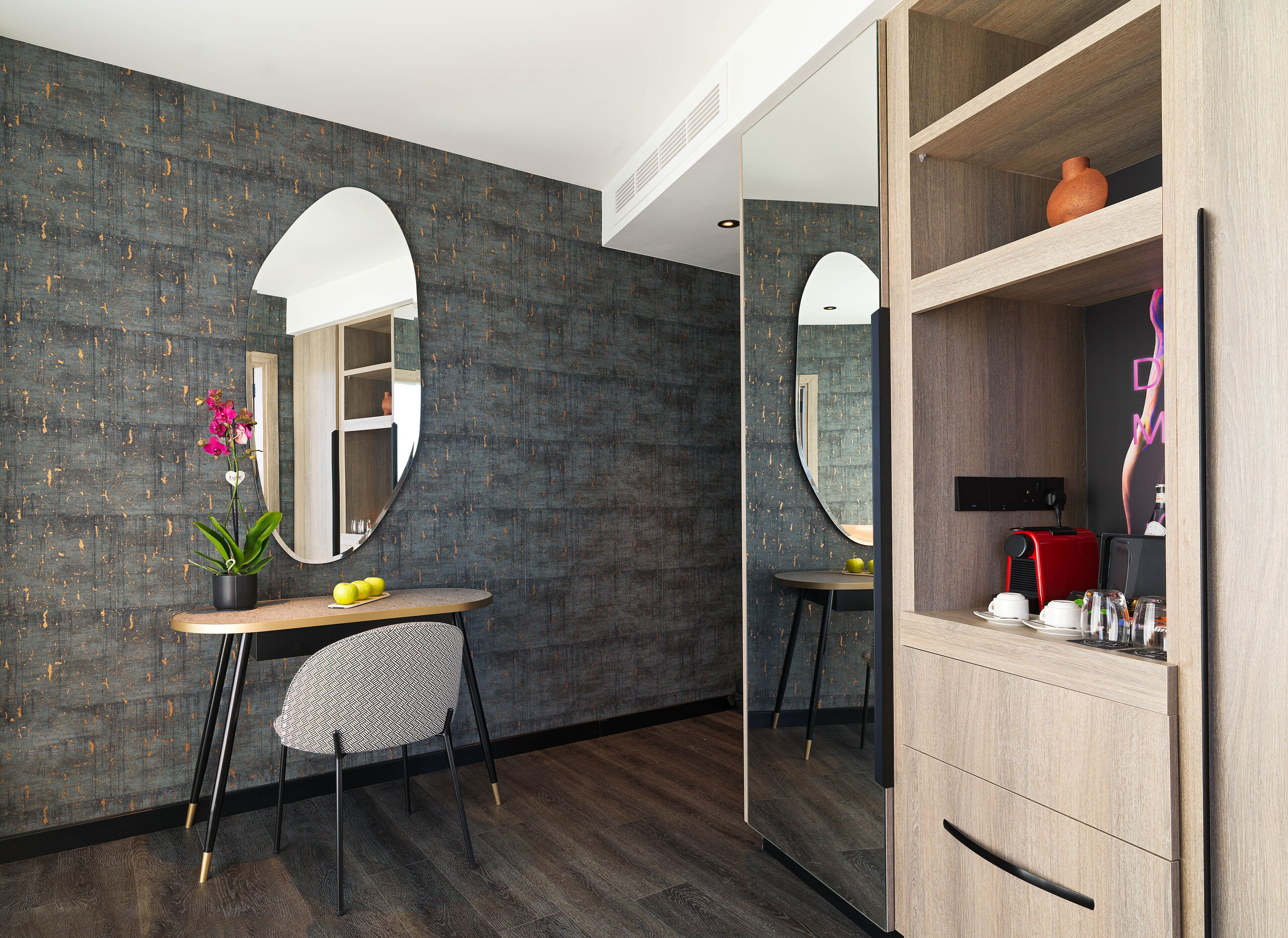 A modern room with dark textured walls, a round mirror, a wooden cabinet, and a small table with a chair.