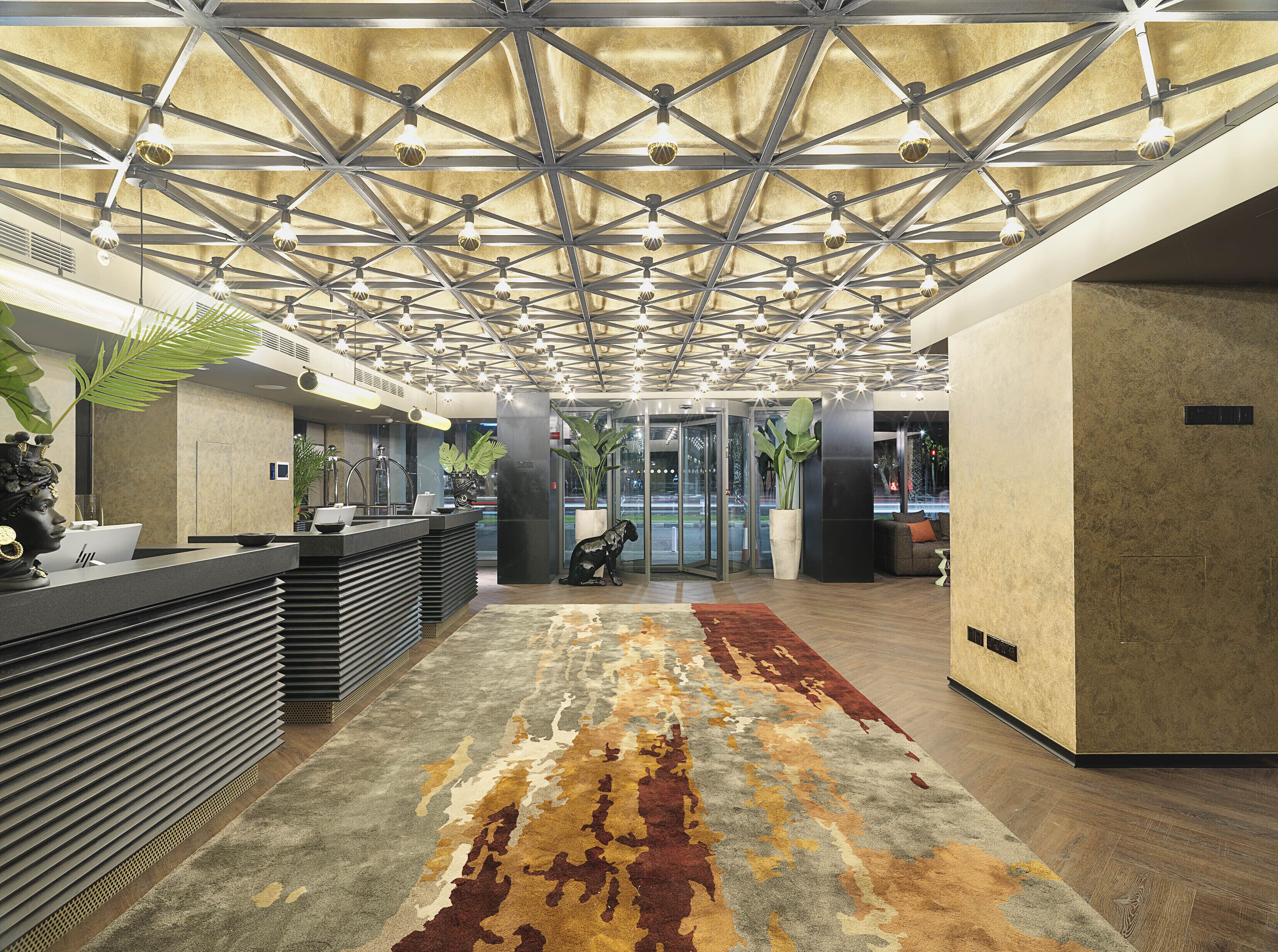 A modern lobby with a geometric ceiling design, a reception desk, and a patterned carpet.