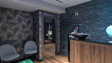 A modern reception area with a dark stone wall, two patterned chairs, a small green table, and a wooden reception desk with a sign.