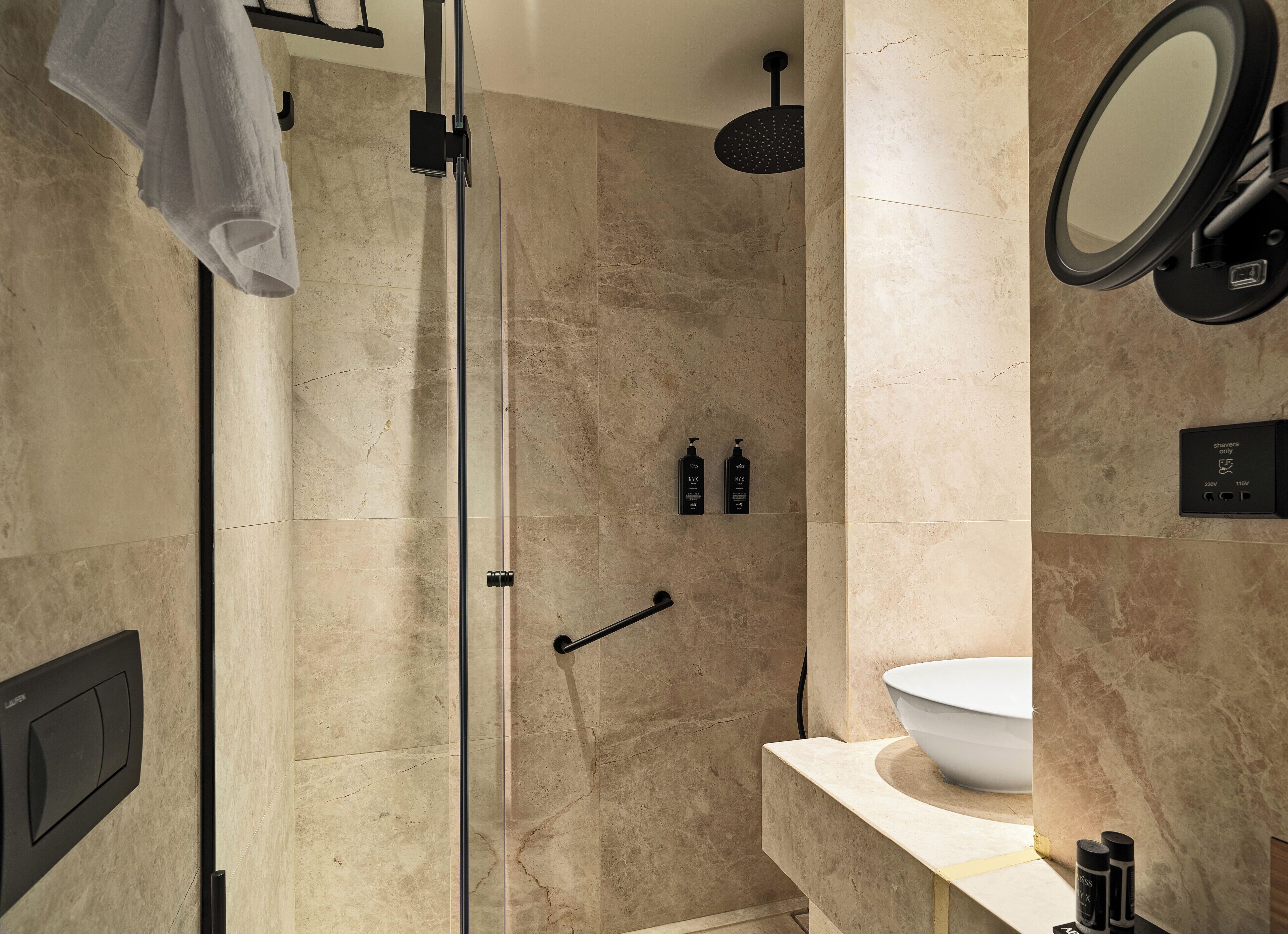A modern bathroom with a glass-enclosed shower, a round mirror, and a white sink.