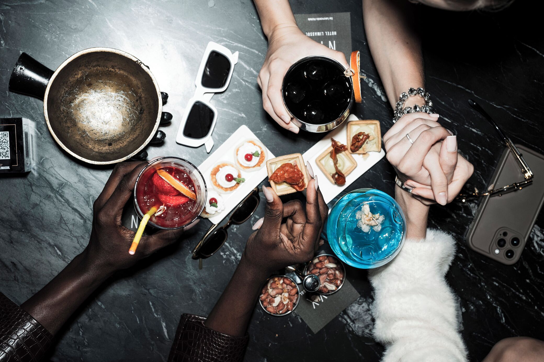 Un groupe de personnes, debout autour d’une table en marbre sombre, tenant des boissons et des plats.