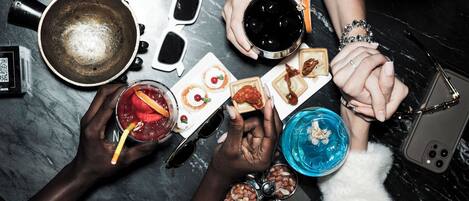 Un groupe de personnes, debout autour d’une table en marbre sombre, tenant des boissons et des plats.