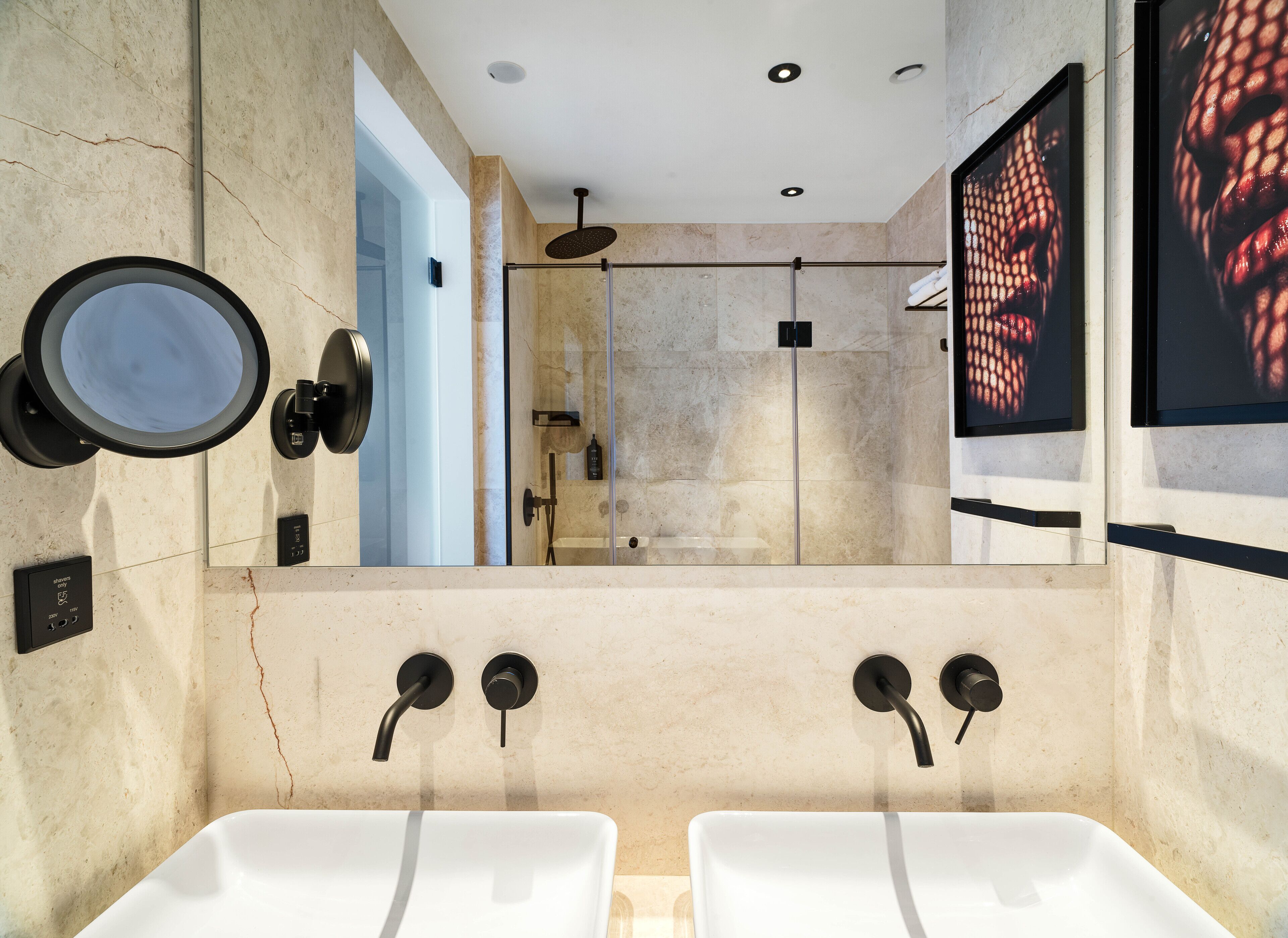 A modern bathroom with two white sinks, a large mirror, and a shower area.