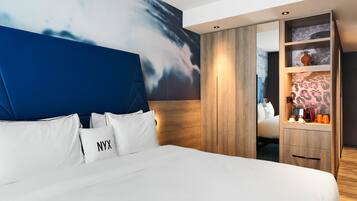 A modern hotel room with a large bed, a wooden wardrobe, and a wall mural.