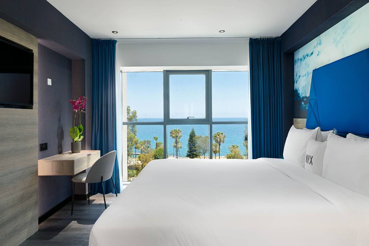 Una habitación de hotel moderna con una cama grande, un escritorio y vista al océano.