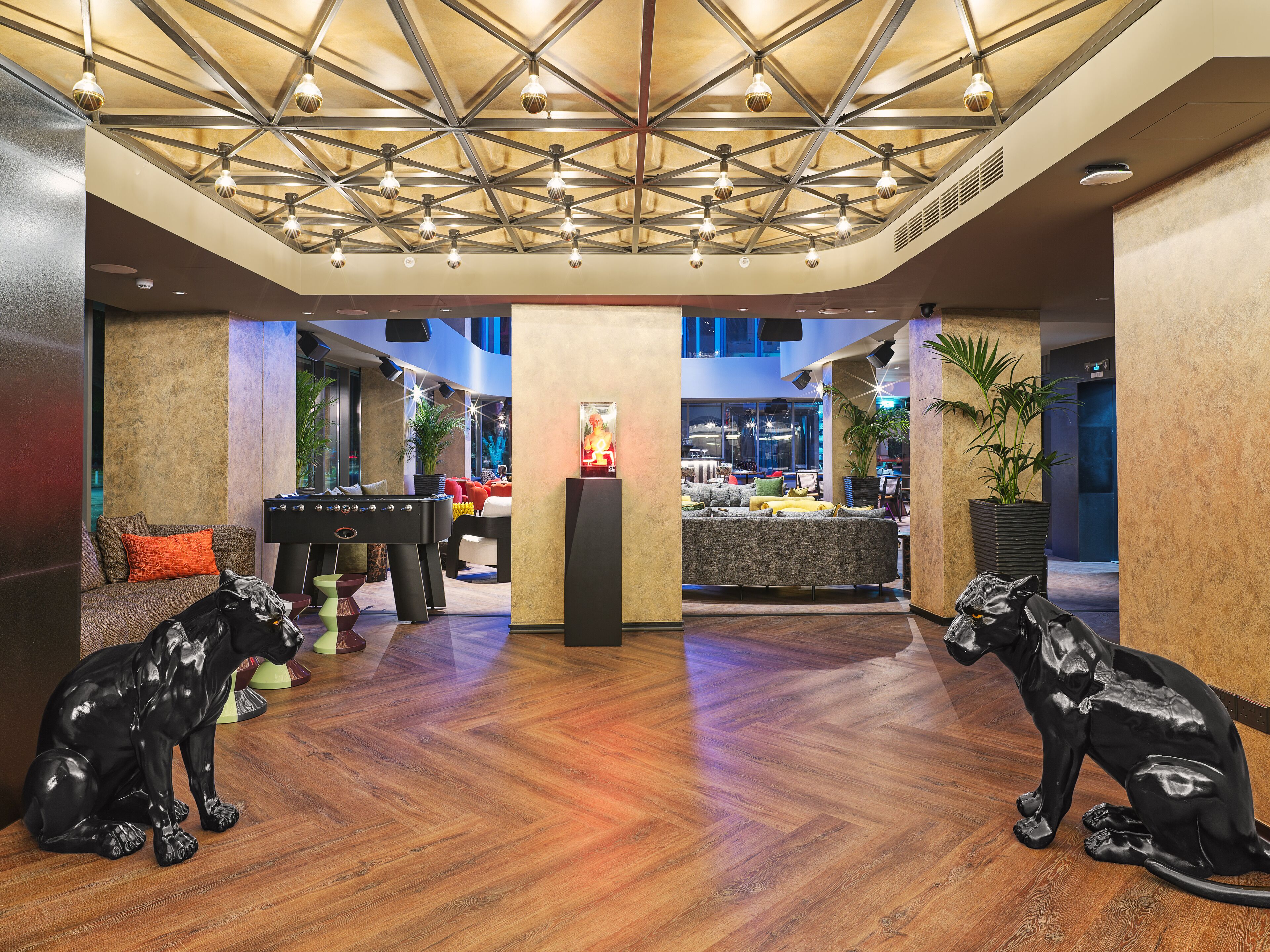 A lobby with a wooden floor, a pool table, and two black dog statues.