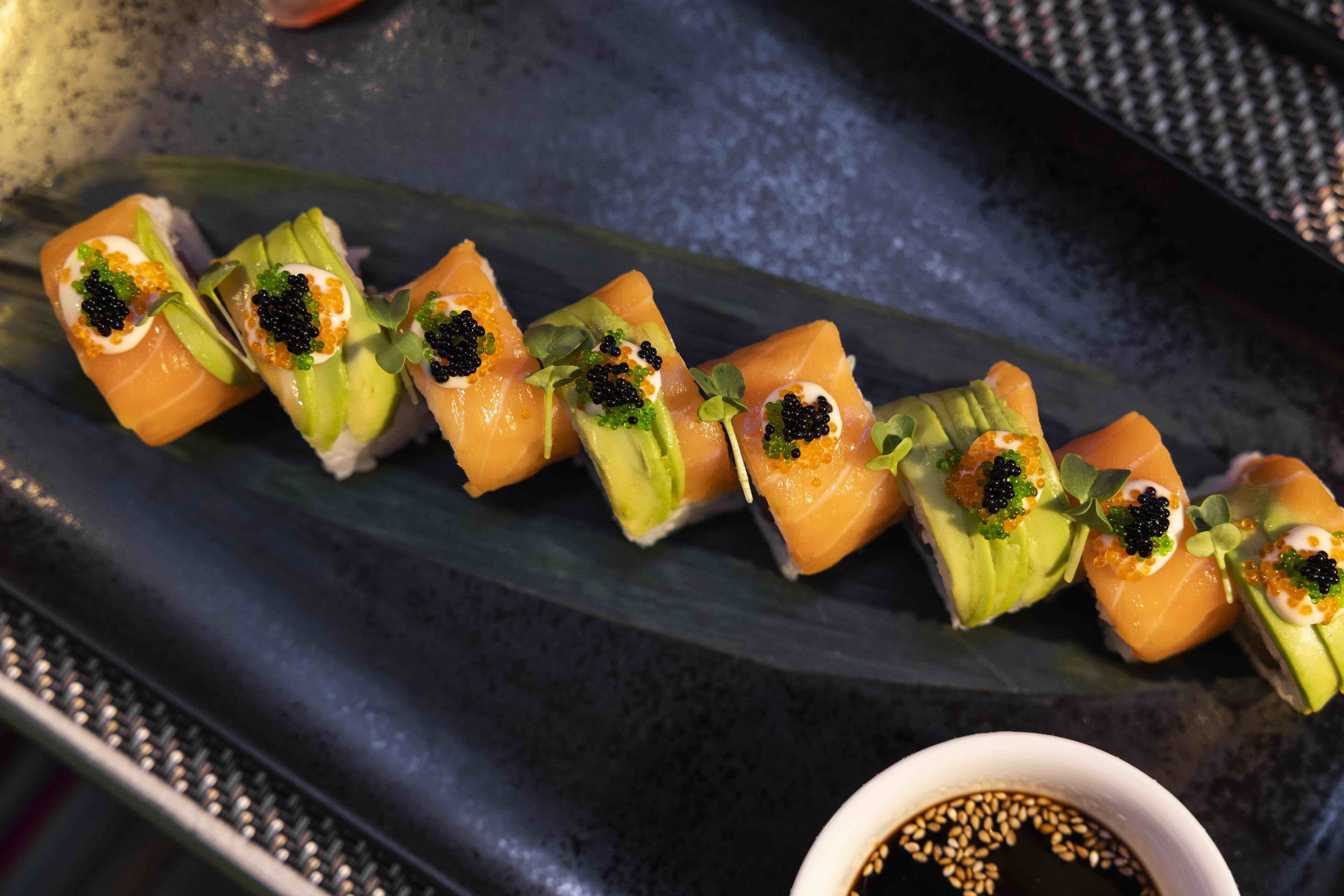 A sushi platter with nigiri and a small bowl of soy sauce.
