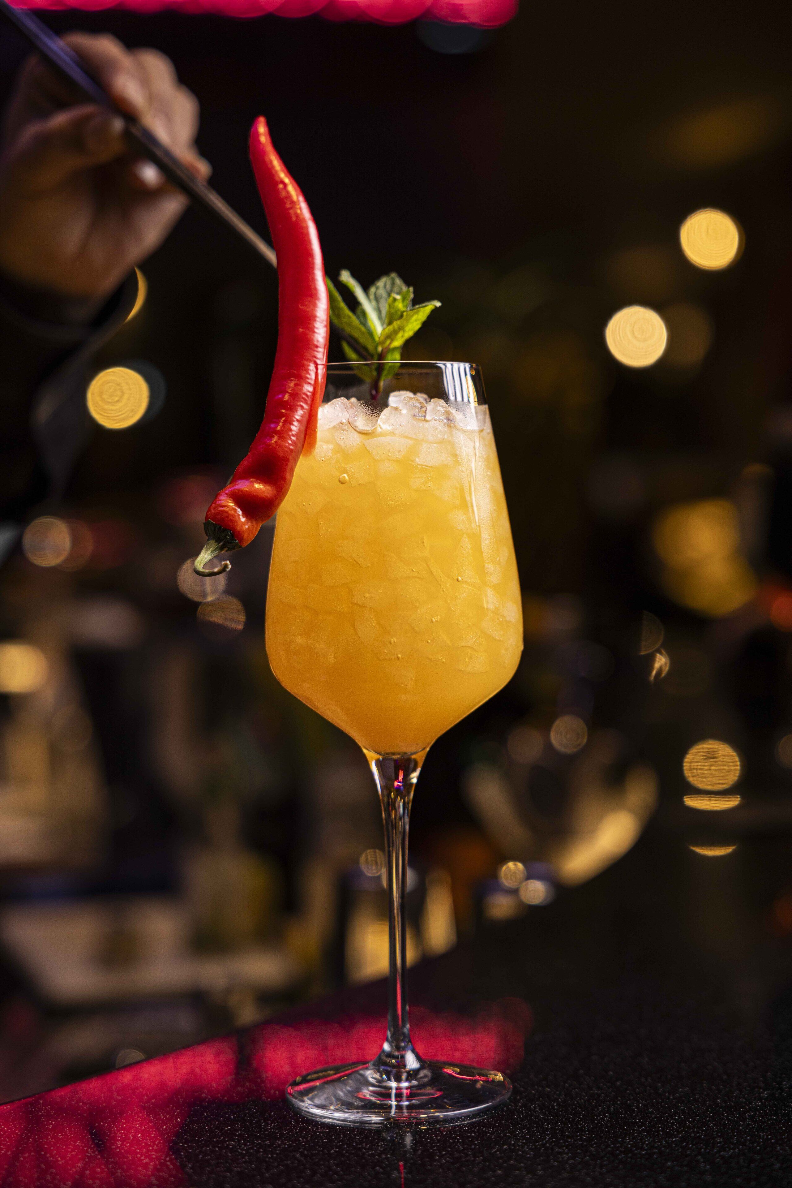 Un cocktail servi dans un grand verre, garni d’un piment rouge et de quelques feuilles de menthe.
