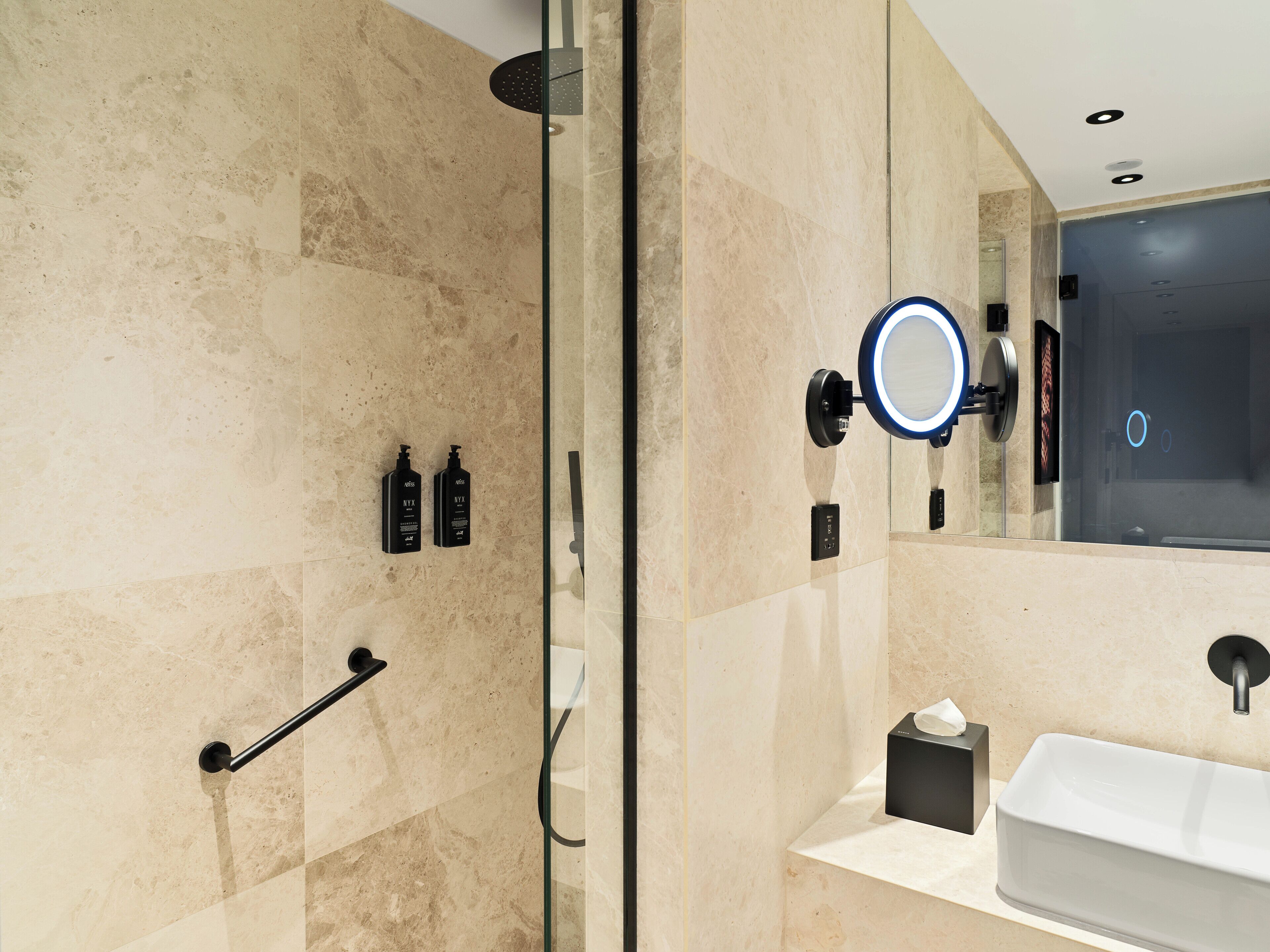Un baño moderno con cabina de ducha de vidrio, un lavabo con espejo y artículos de aseo en la pared.