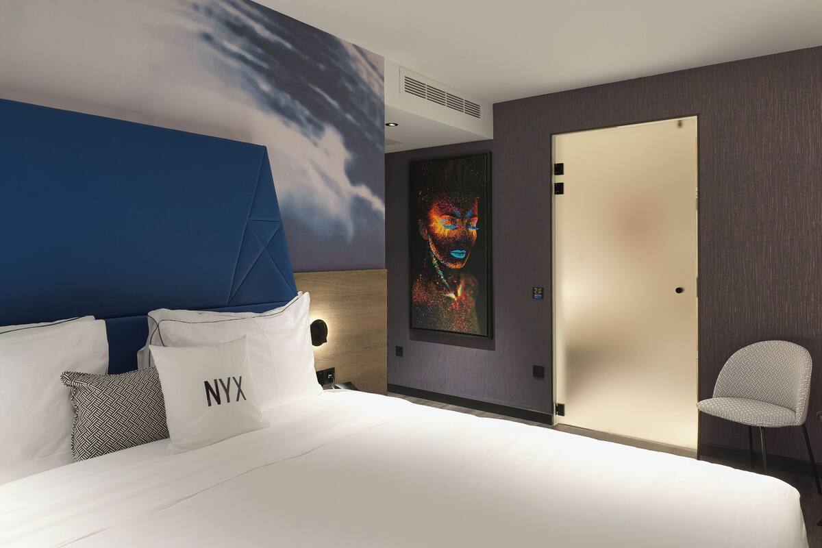 Una habitación de hotel moderna con una cama grande, un cabecero azul, una obra de arte enmarcada y una puerta con manija.