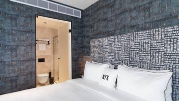 A hotel room with a large bed, a headboard with a cityscape pattern, and a bathroom visible through an open door.