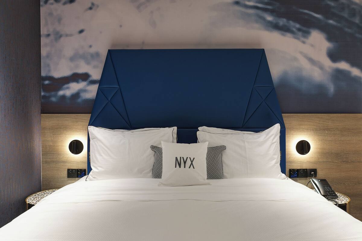 Una habitación de hotel moderna con una cama grande, un cabecero con motivos geométricos y un mural en la pared.