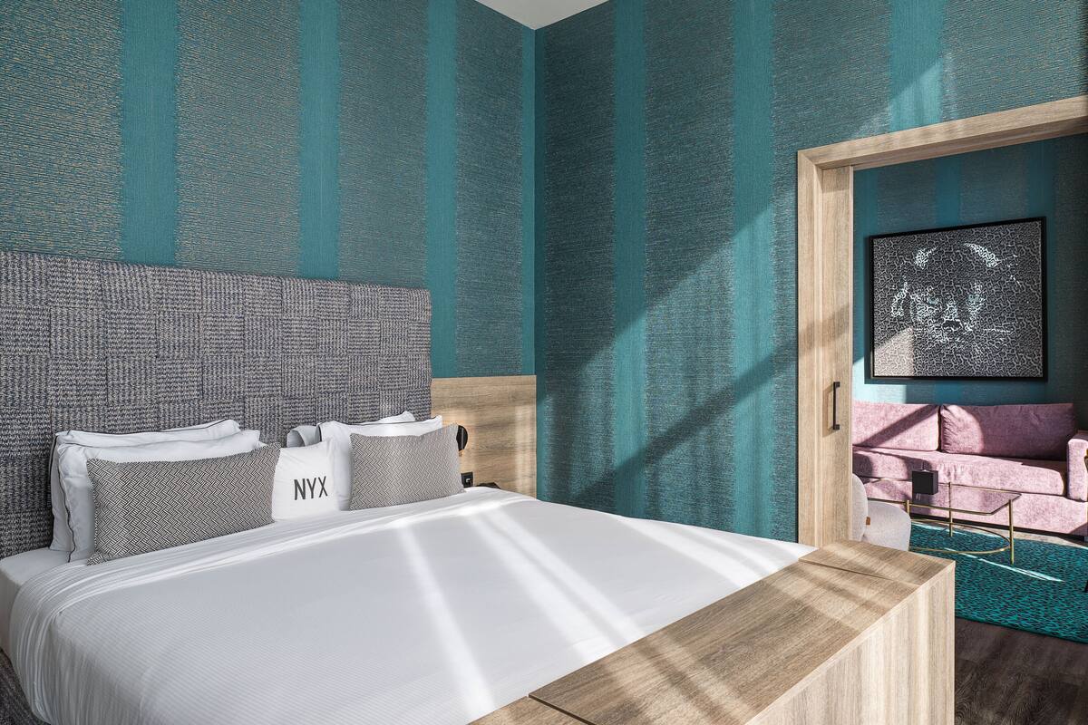 Una habitación de hotel moderna con una cama grande, cabecera de madera y pared a rayas azul verdosas.