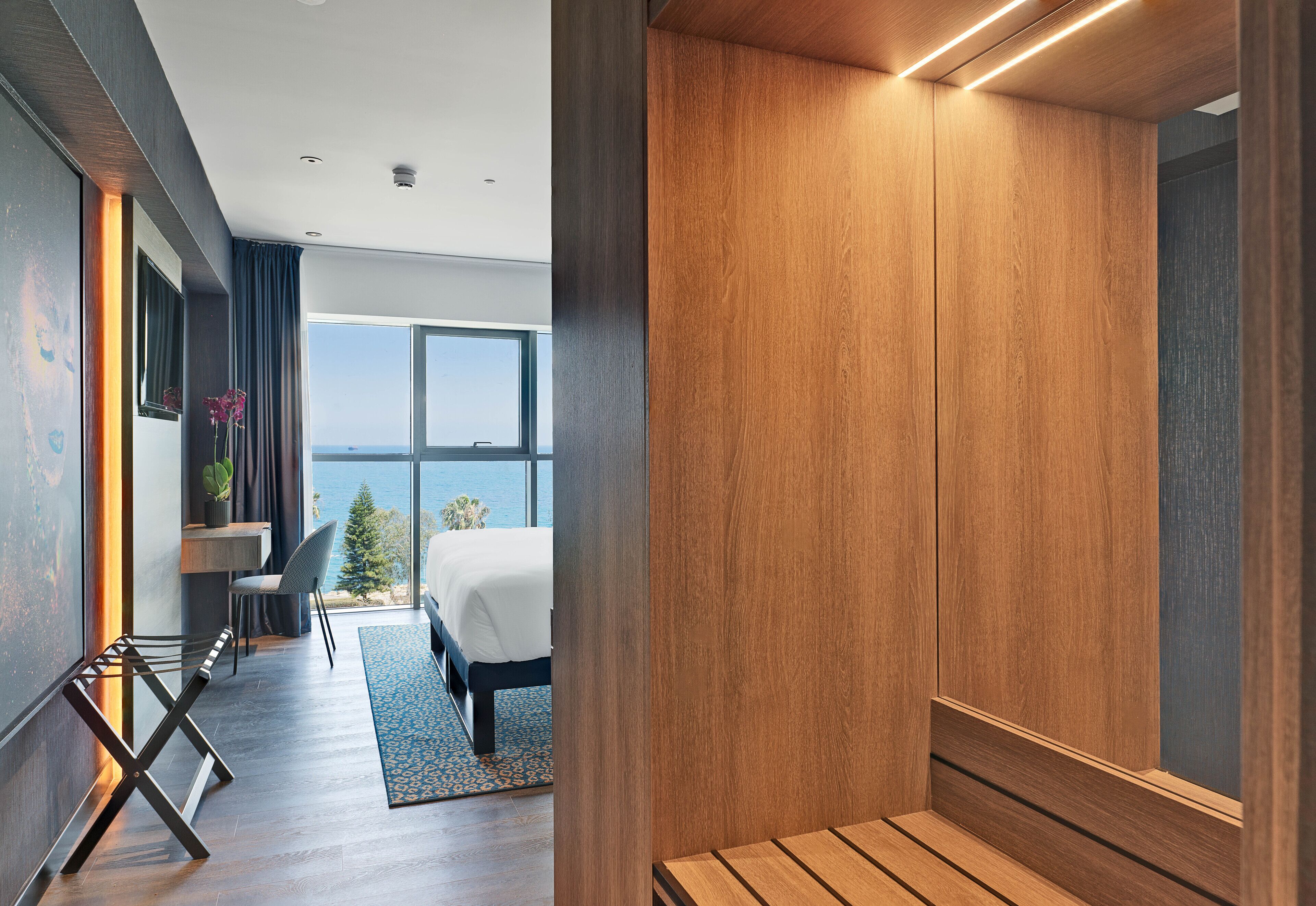 A modern hotel room with a large window, a bed, a desk, and a chair.