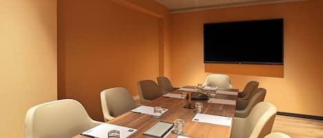 A conference room with a long table, chairs, a flat-screen TV, and a wooden floor.