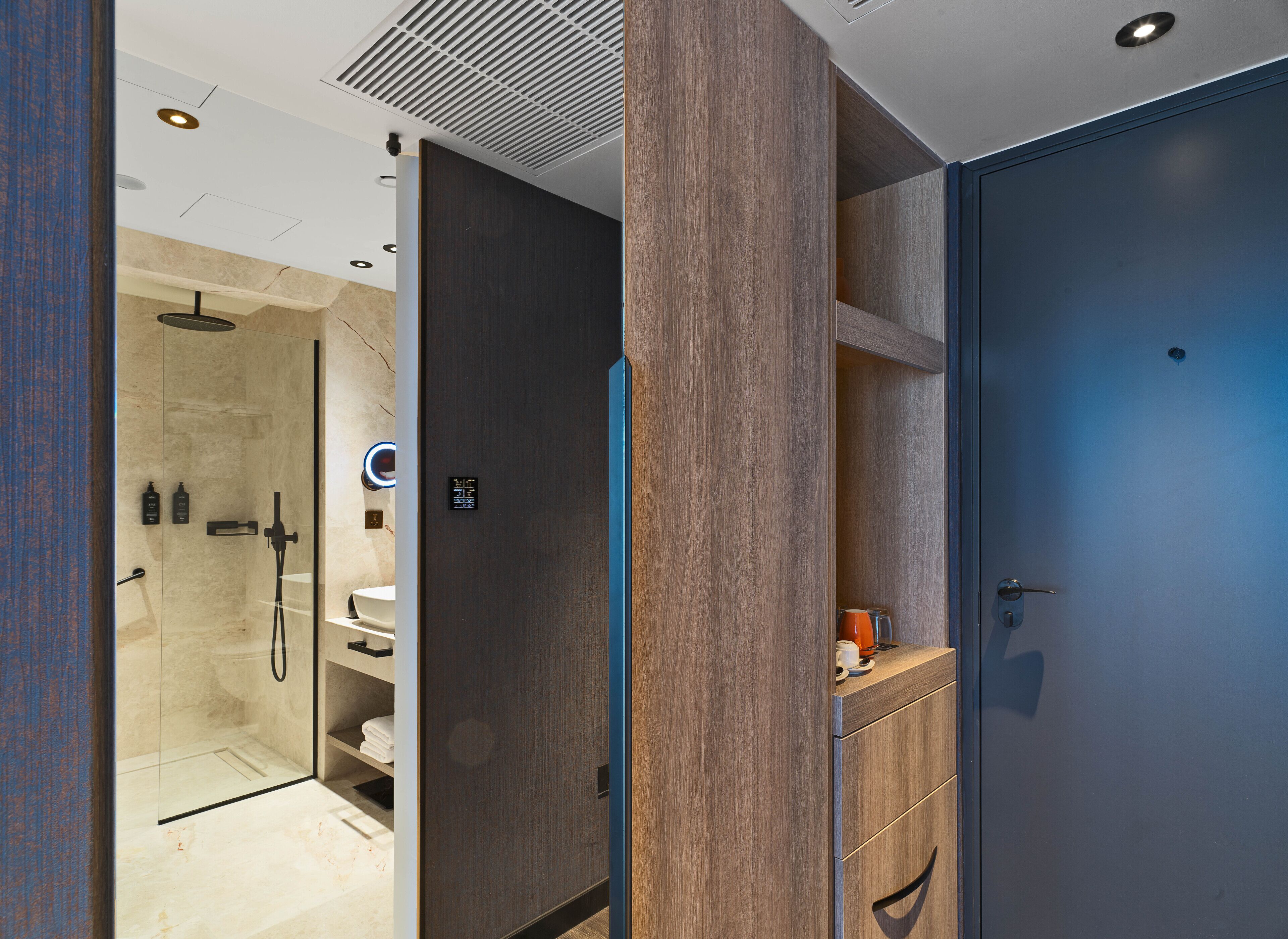 Un baño moderno con cabina de ducha de vidrio, tocador de madera y puerta azul.
