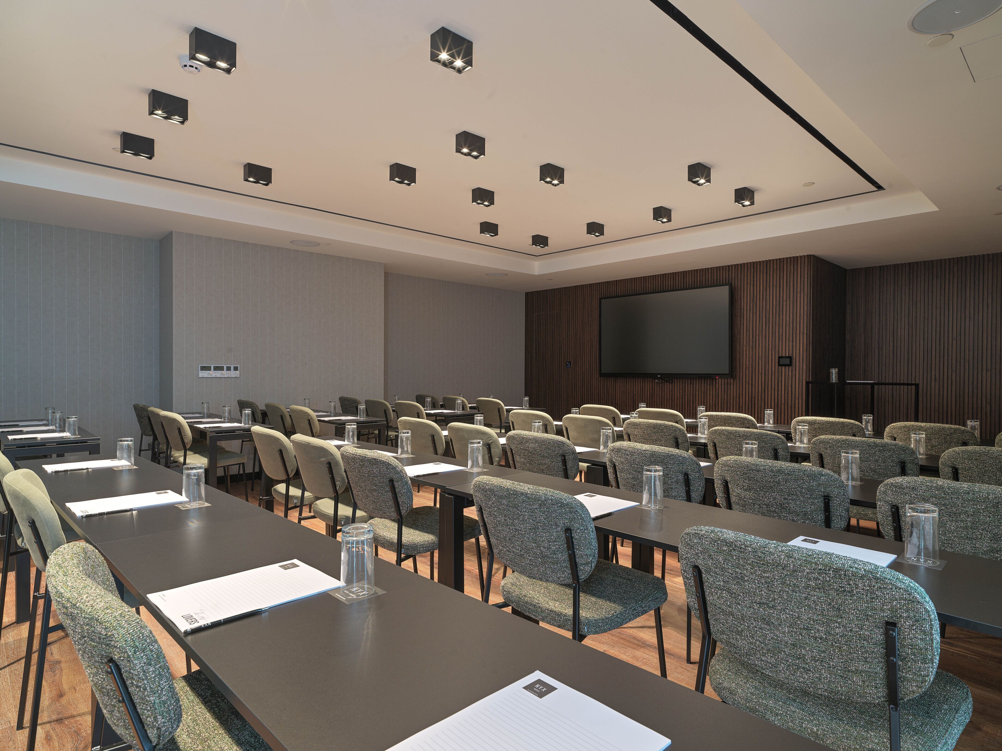 Un salón de conferencias con varias mesas y sillas, una pantalla grande y luces empotradas en el techo.
