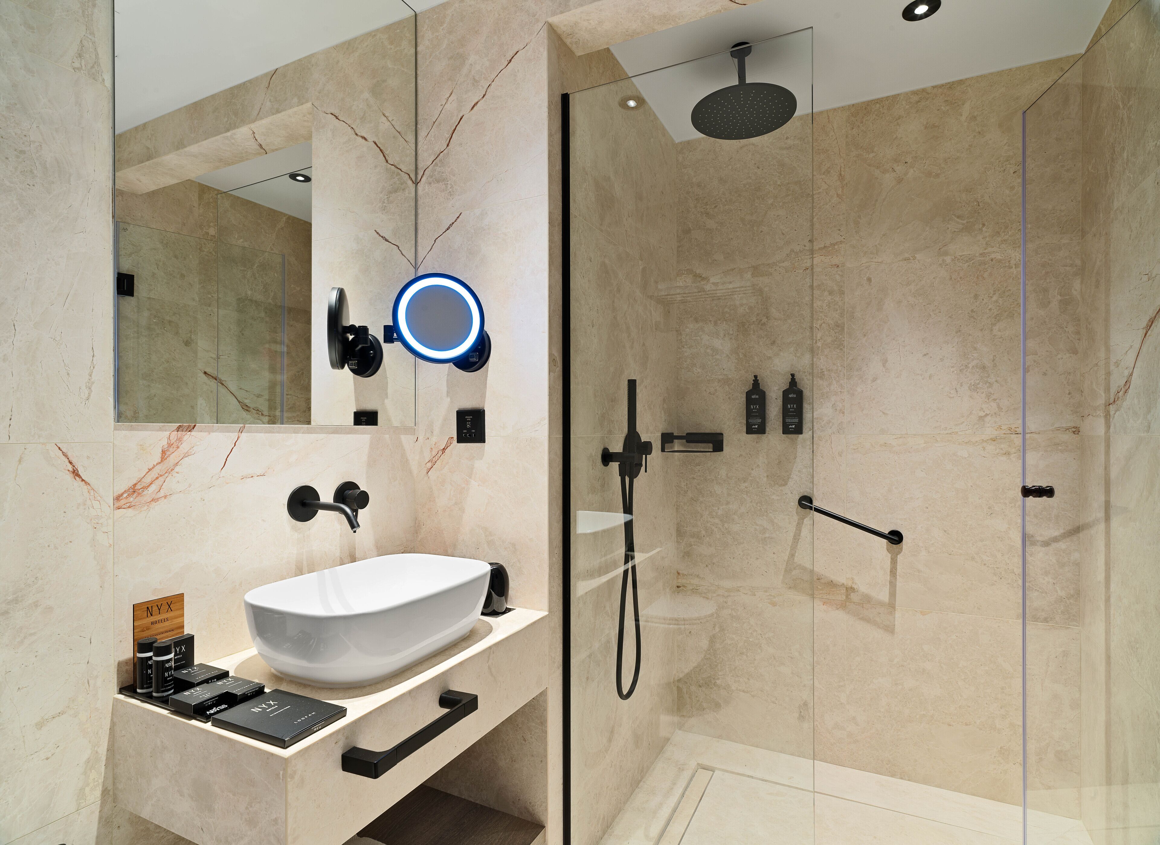A modern bathroom with a large mirror, a vessel sink, a handheld showerhead, and a glass-enclosed shower.