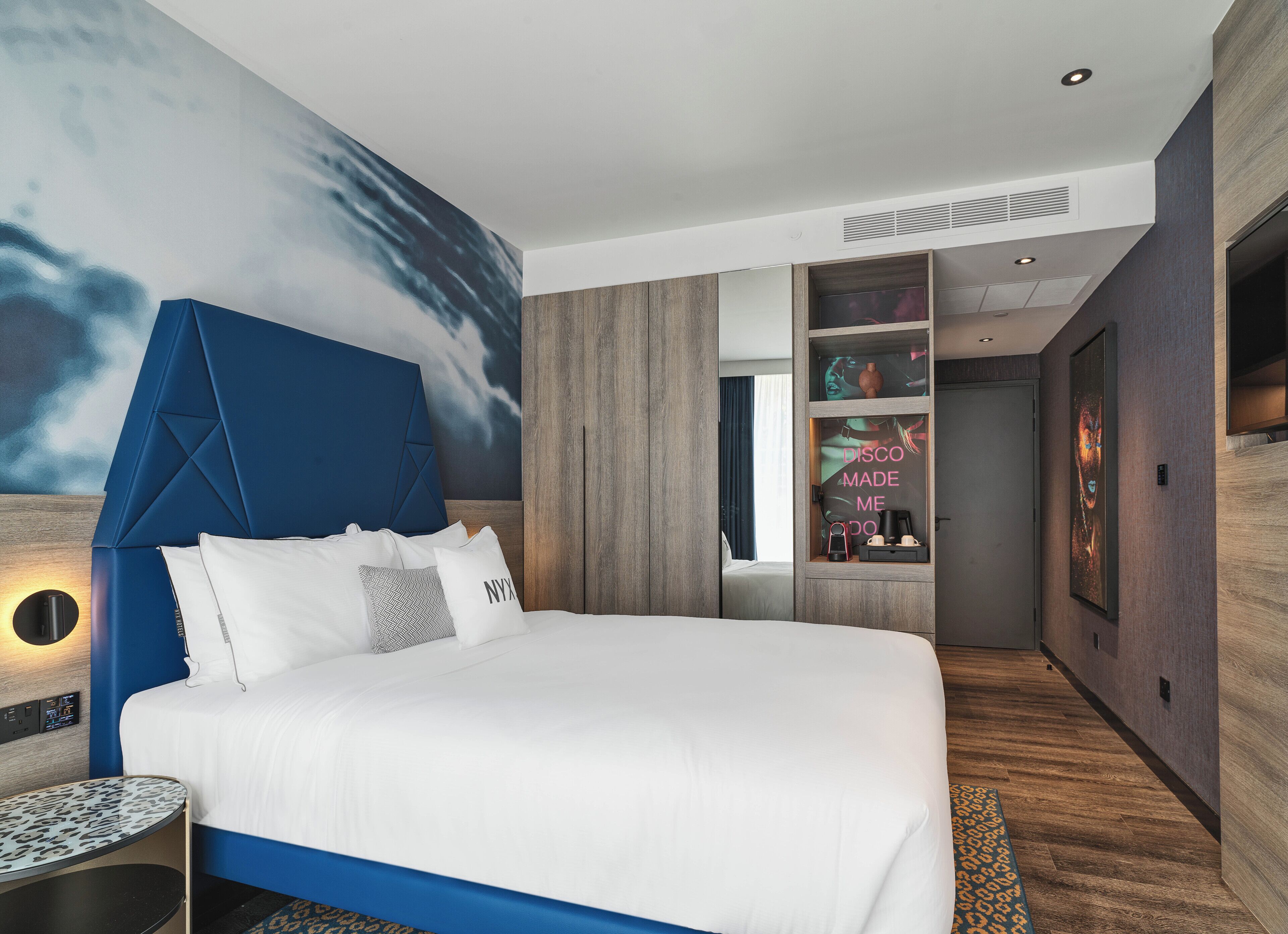 A modern hotel room with a large bed, a wall-mounted TV, and a built-in wardrobe.