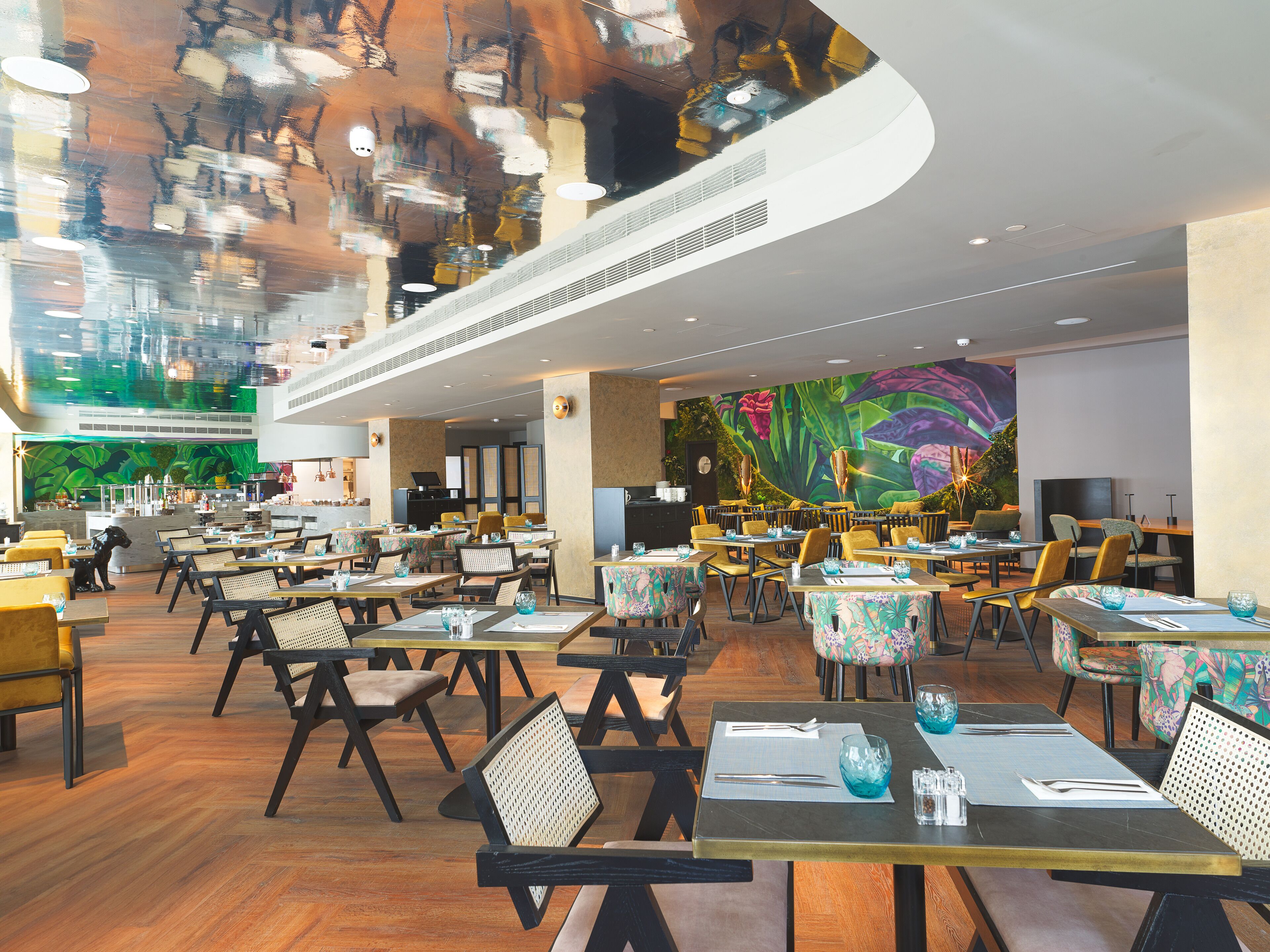 Un restaurant spacieux doté de plusieurs espaces de restauration, de hauts plafonds et d’une fresque murale colorée.