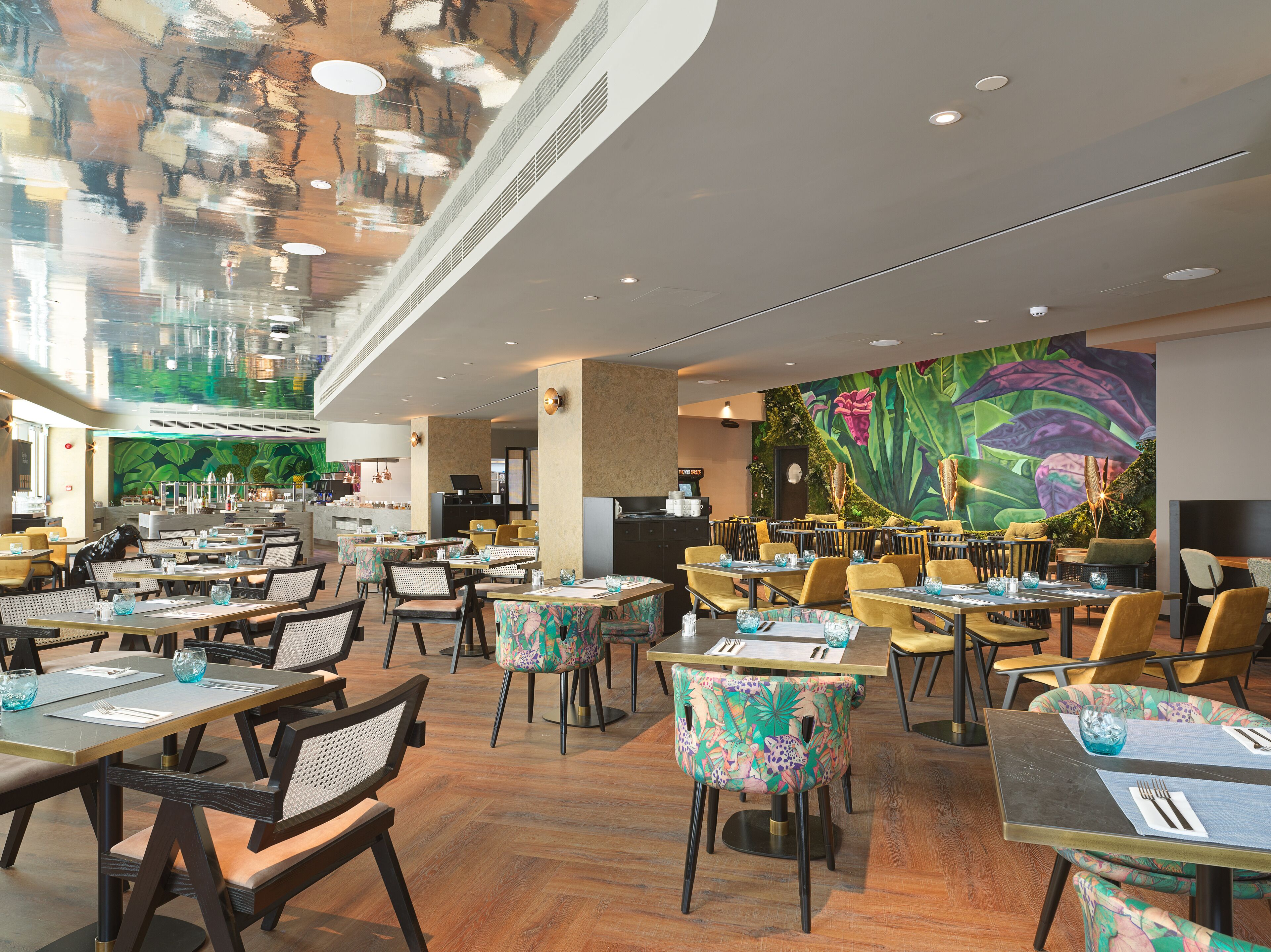 A spacious restaurant with multiple dining areas, including a bar and a seating area with a mural.
