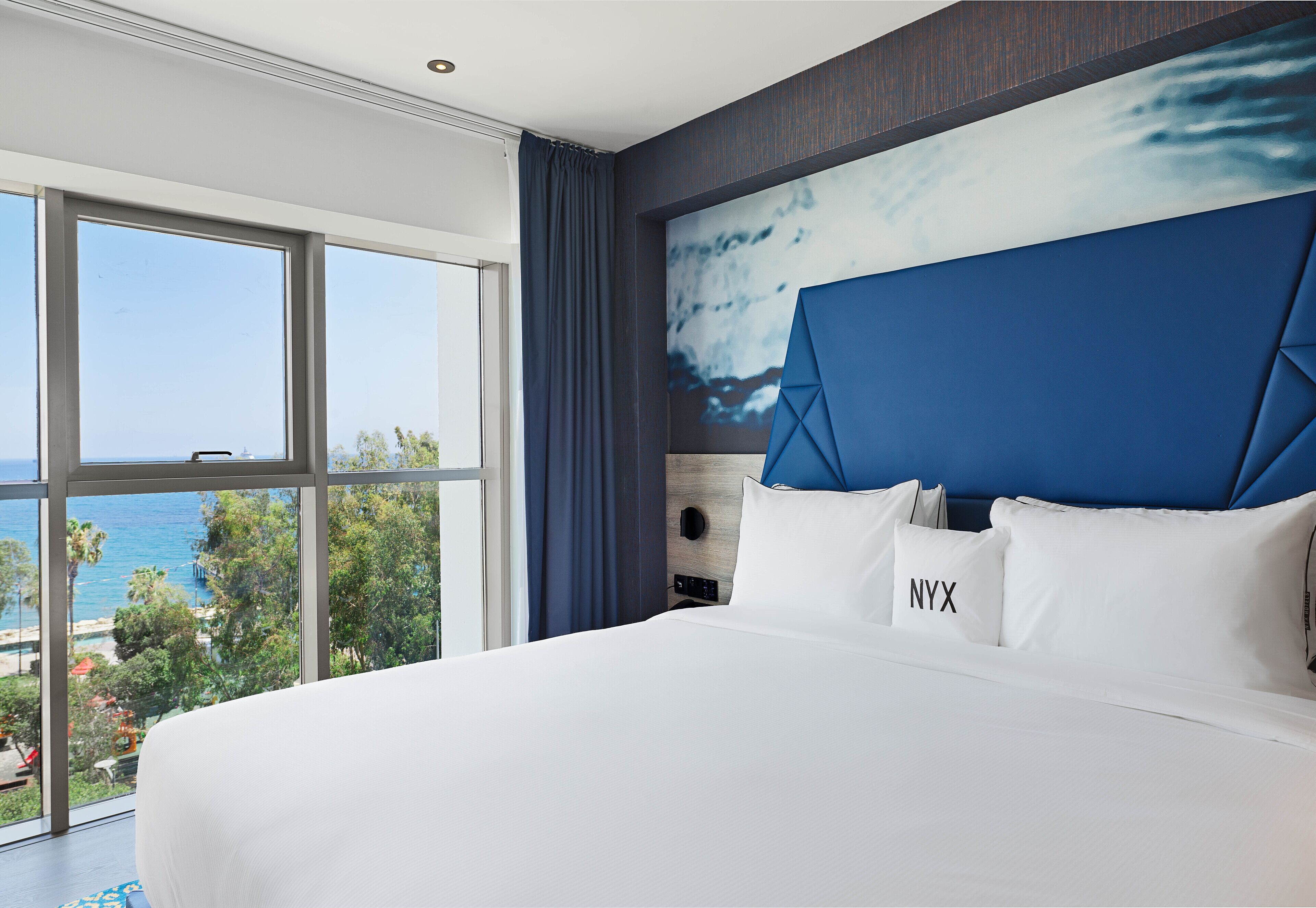 Une chambre d’hôtel avec un grand lit, une vue sur l’océan et une tête de lit moderne.