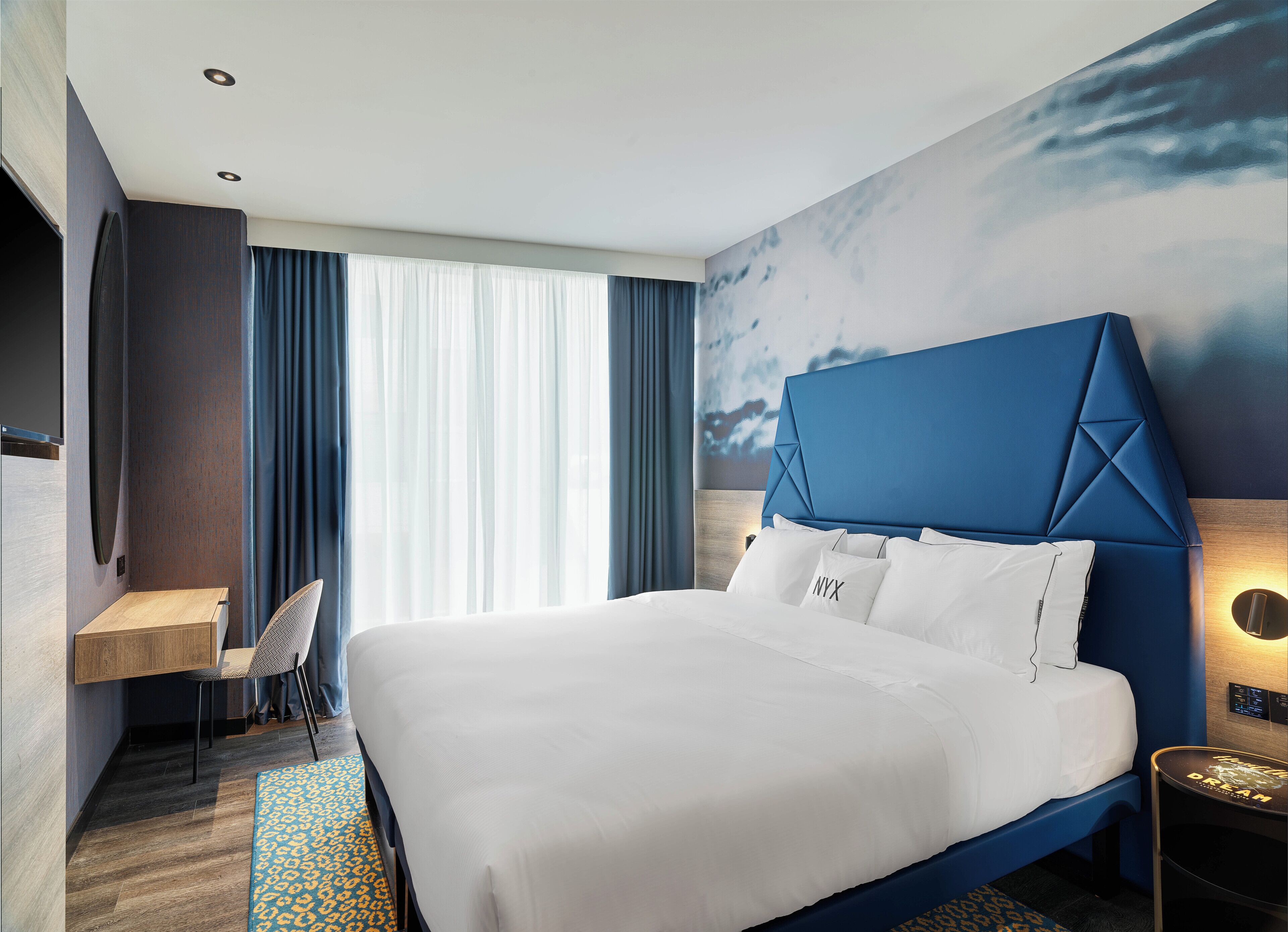 A modern hotel room with a large bed, a desk, and a chair.