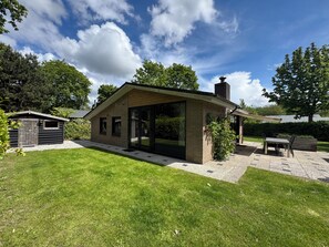 Een modern huis met een grote glazen deur, een klein tuinhuisje en een patio.