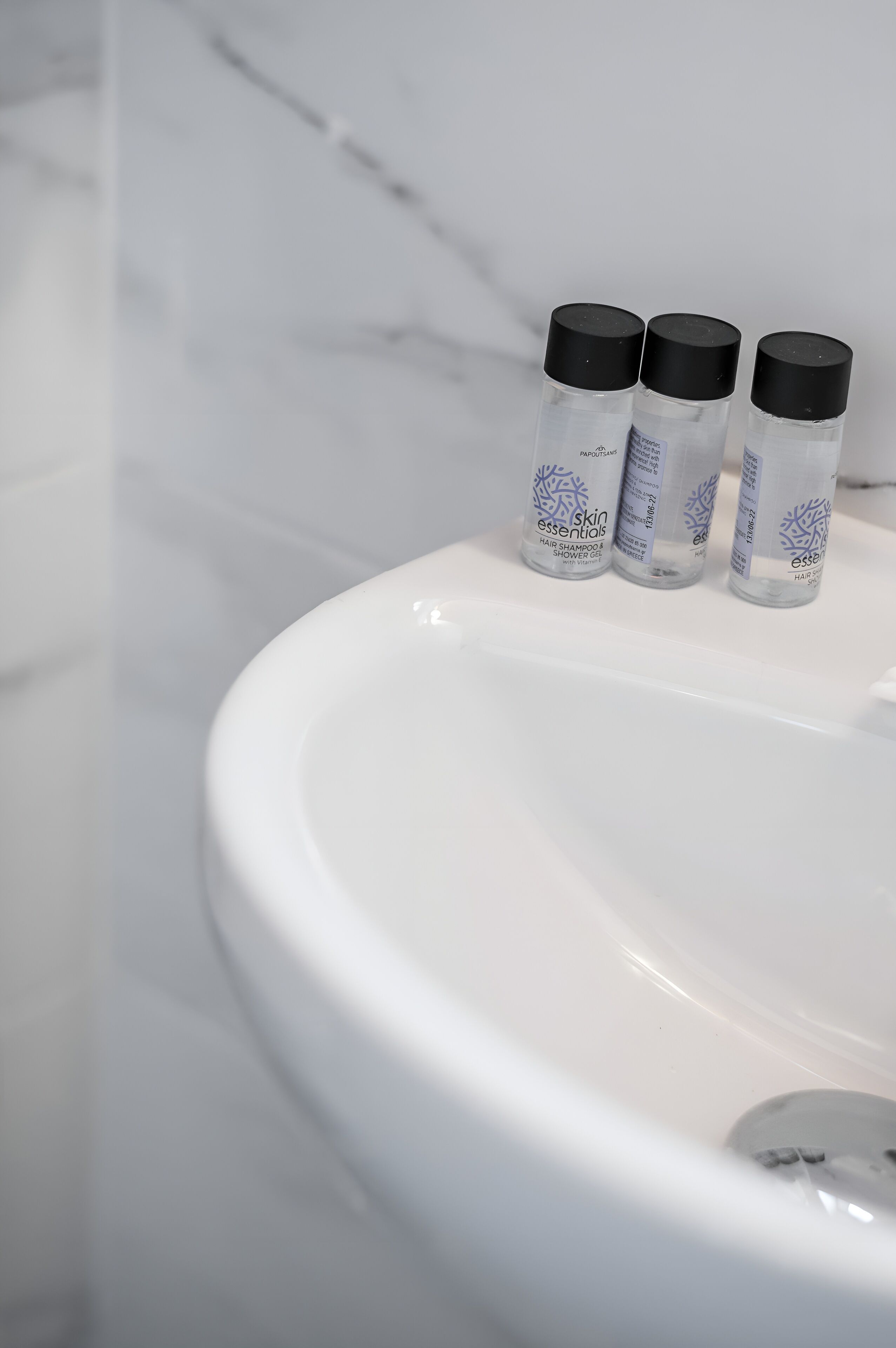 A bathroom sink with three bottles of skin essentials hair shampoo and shower gel.