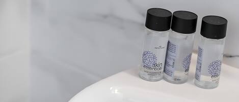 A bathroom sink with three bottles of skin essentials hair shampoo and shower gel.