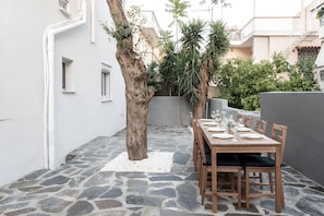 An outdoor dining area with a stone floor, a wooden table set for four, and a tree in the center.