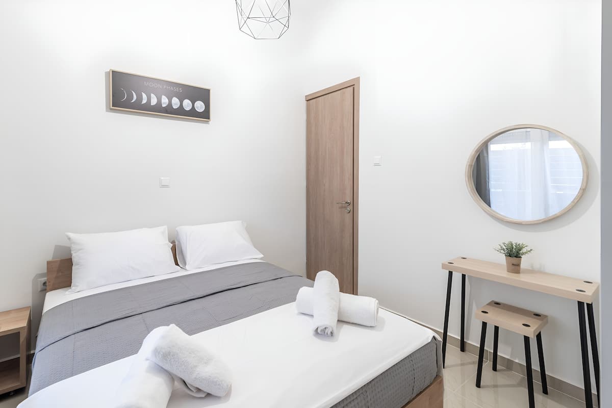 A modern bedroom with a bed, a wooden door, a round mirror, and a wall-mounted picture of moon phases.