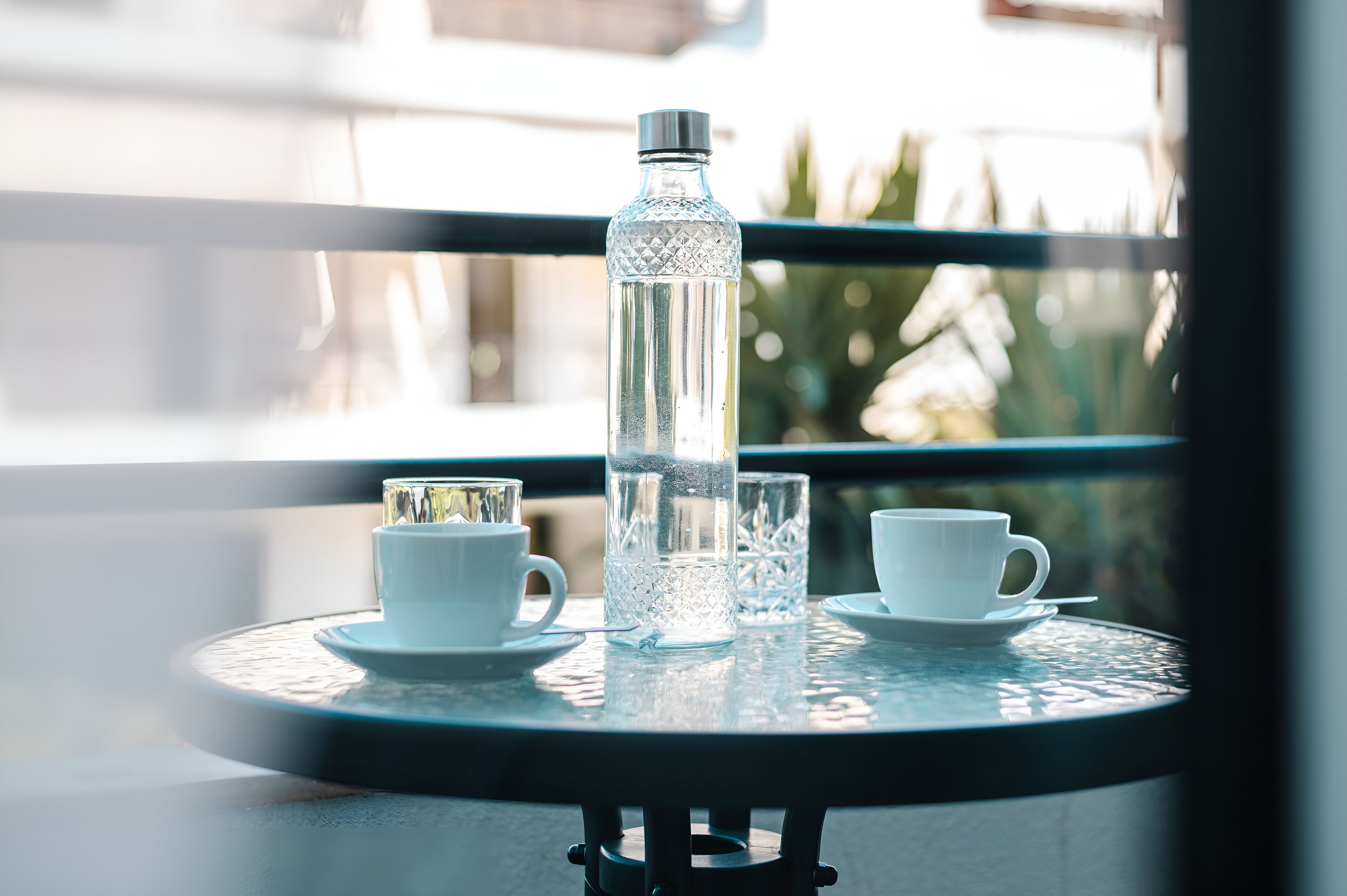 A round glass table with a water bottle, two white cups, and a glass on it.