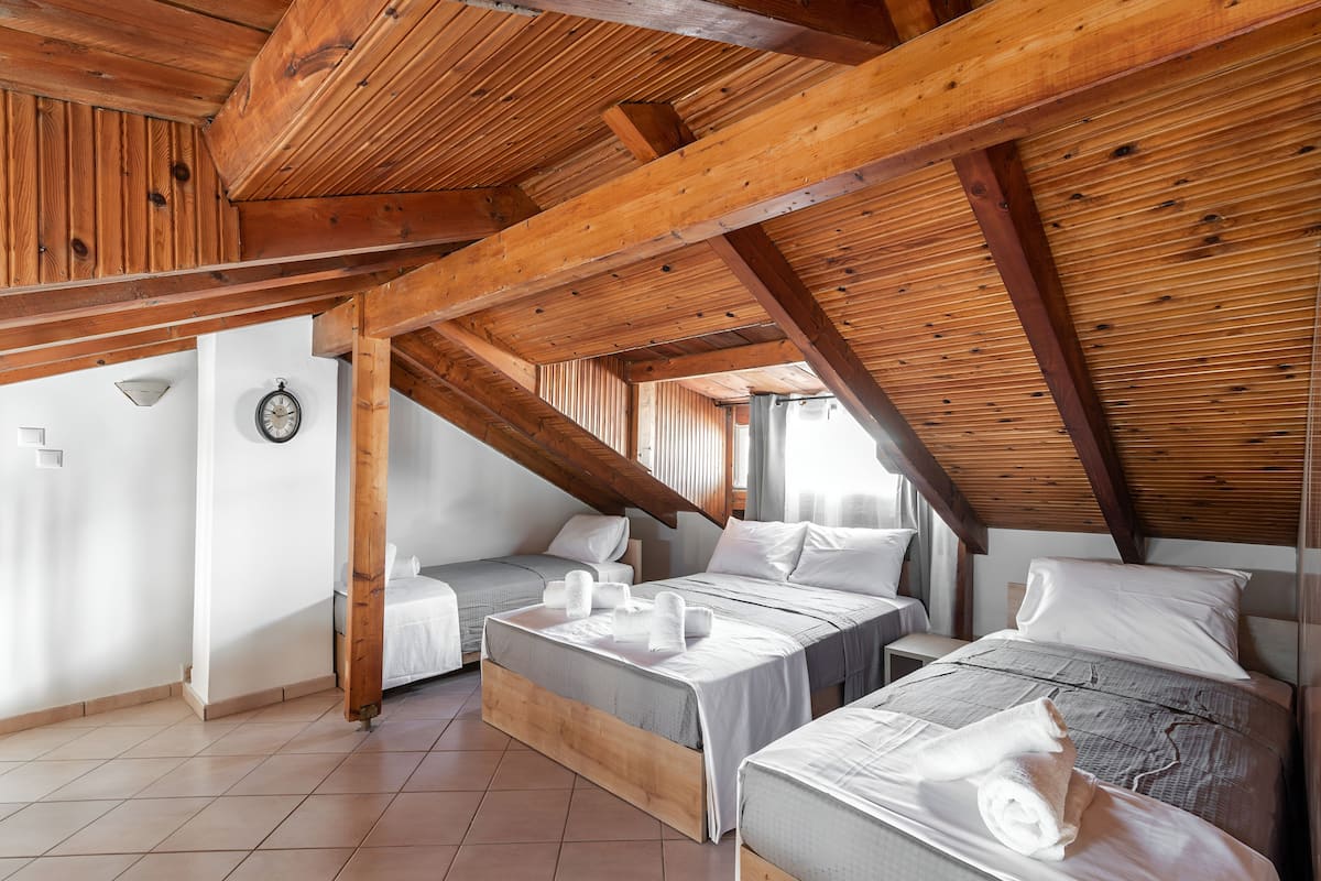 A room with a sloped ceiling, wooden beams, and two beds with white bedding.