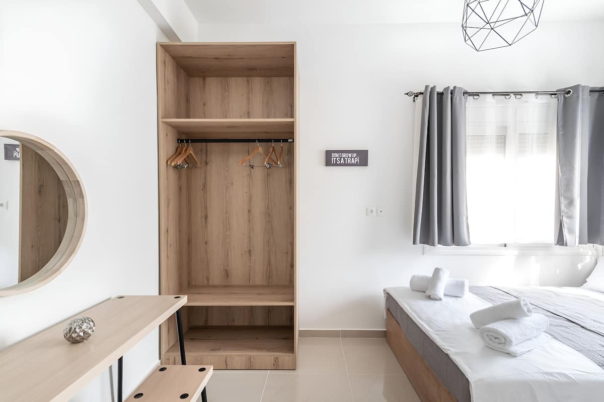 A modern hotel room with a wooden wardrobe, a bed with neatly folded towels, a bedside table with a decorative item, and a sign on the wall.
