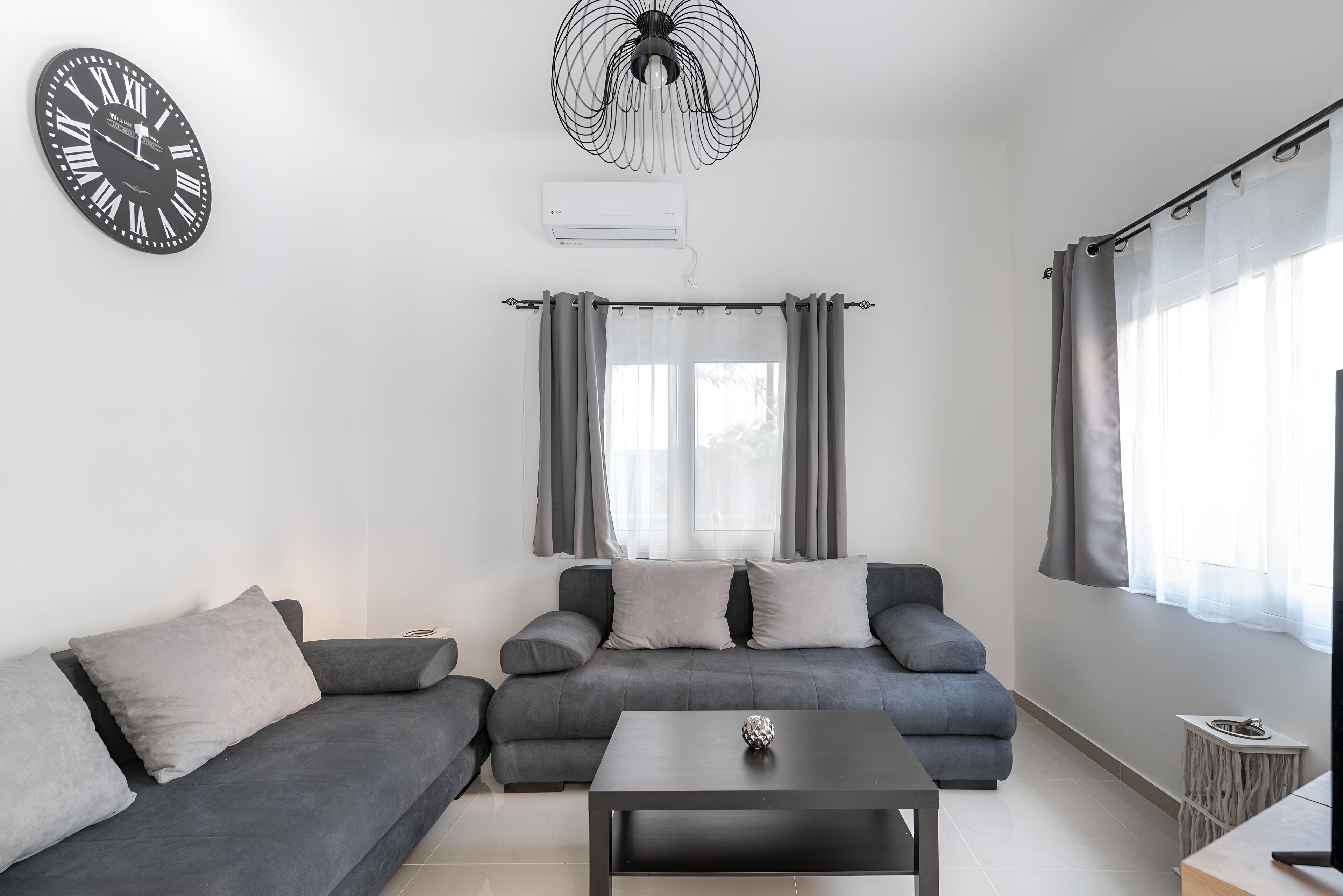 Una sala de estar moderna con un sofá gris, una mesa de centro negra y un reloj de pared.