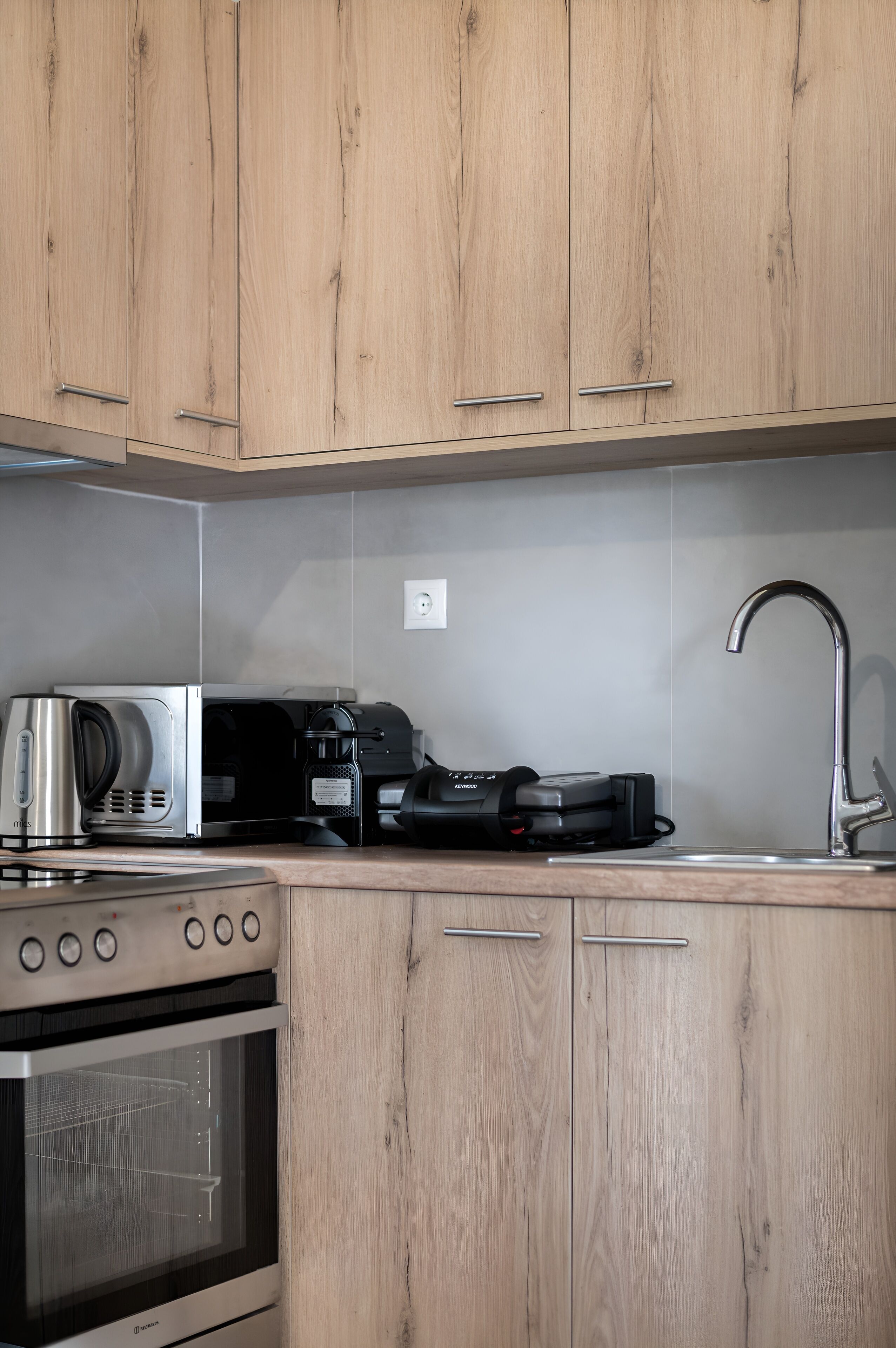 A kitchen with wooden cabinets, a stainless steel kettle, a coffee maker, and a built-in oven.