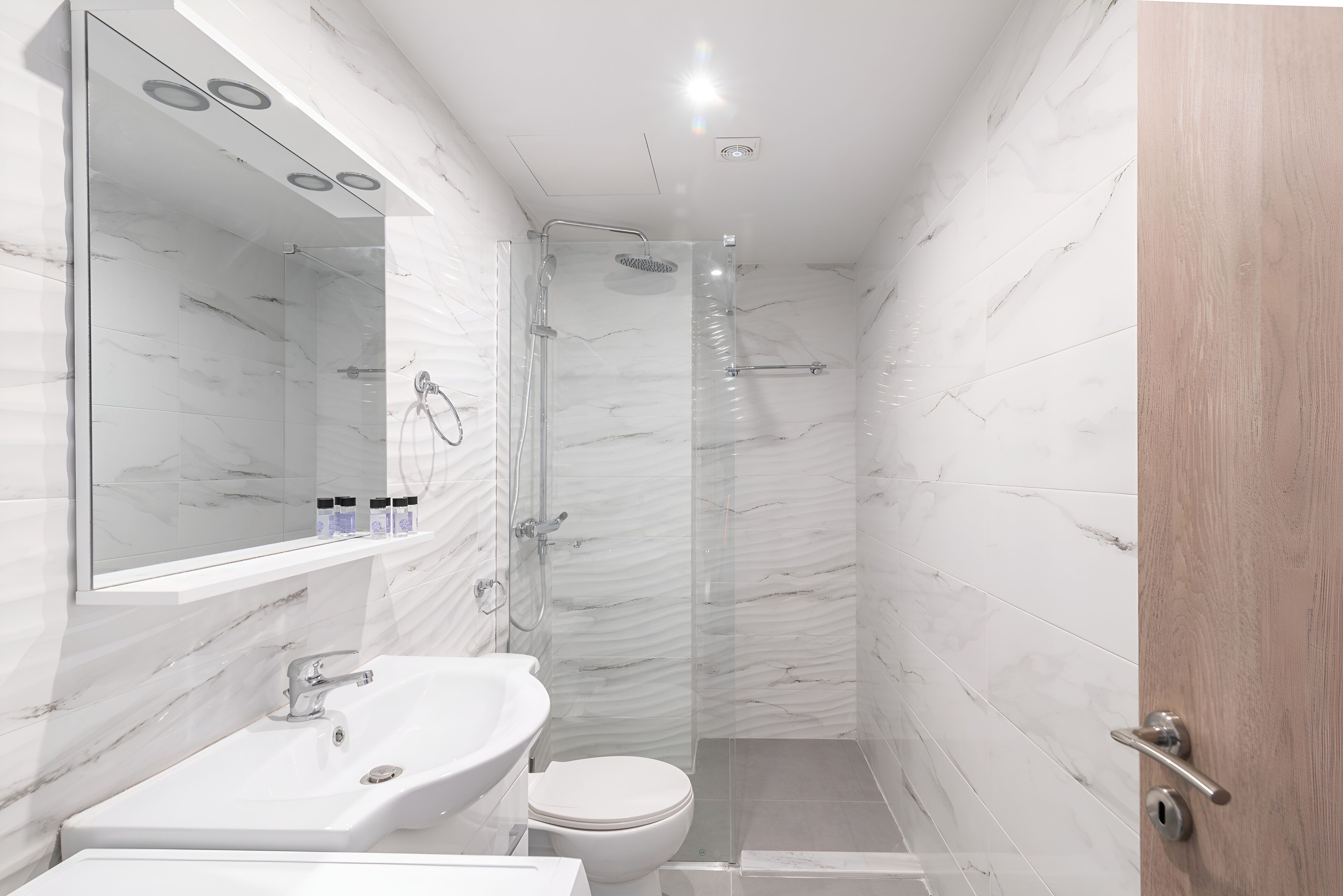 Un baño moderno con ducha envuelta en vidrio, un lavamanos blanco y un inodoro.