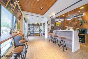 Un área de bar moderna con suelo de madera, una barra con taburetes y varias decoraciones, incluyendo un reloj y cuadros enmarcados.
