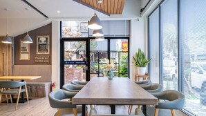 Un moderno comedor con una mesa de madera larga, varias sillas, iluminación colgante y ventanas amplias con persianas.