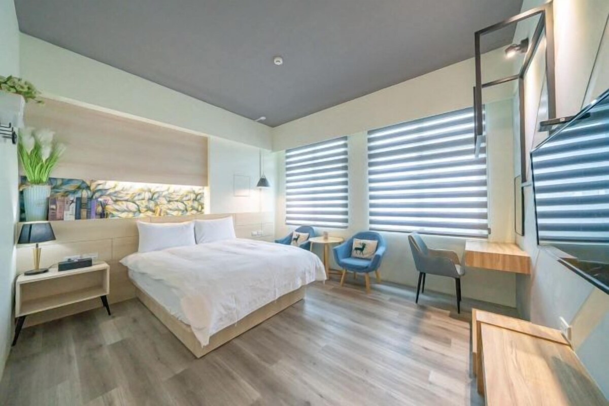 A modern hotel room with a large bed, a desk, two chairs, and a small table.
