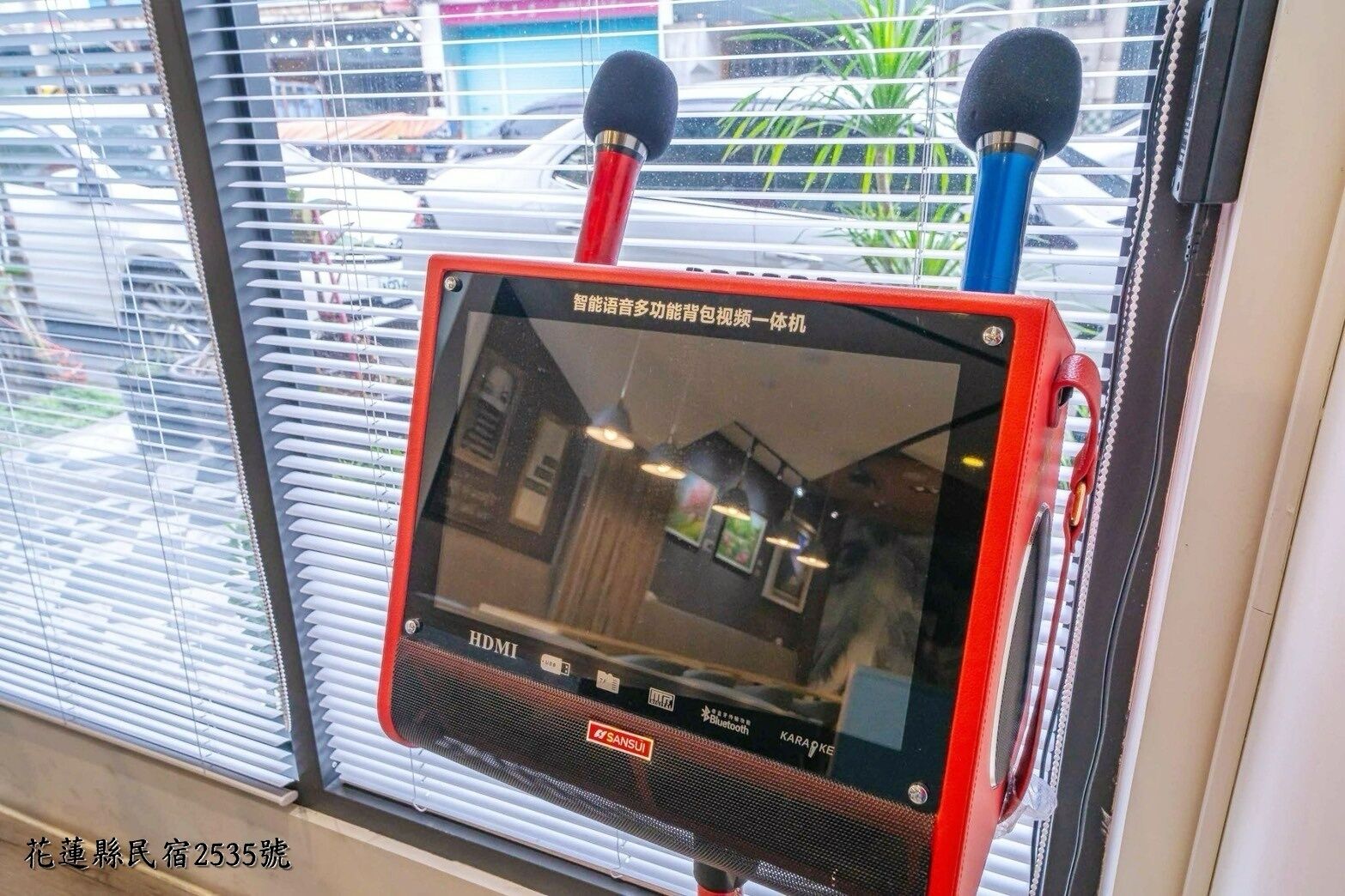A karaoke machine with a screen, Bluetooth, and karaoke features, mounted on a window with blinds.