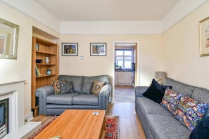 Cozy living room with a fireplace, sofa, and bookshelf, offering a seamless connection to the adjacent kitchen area.