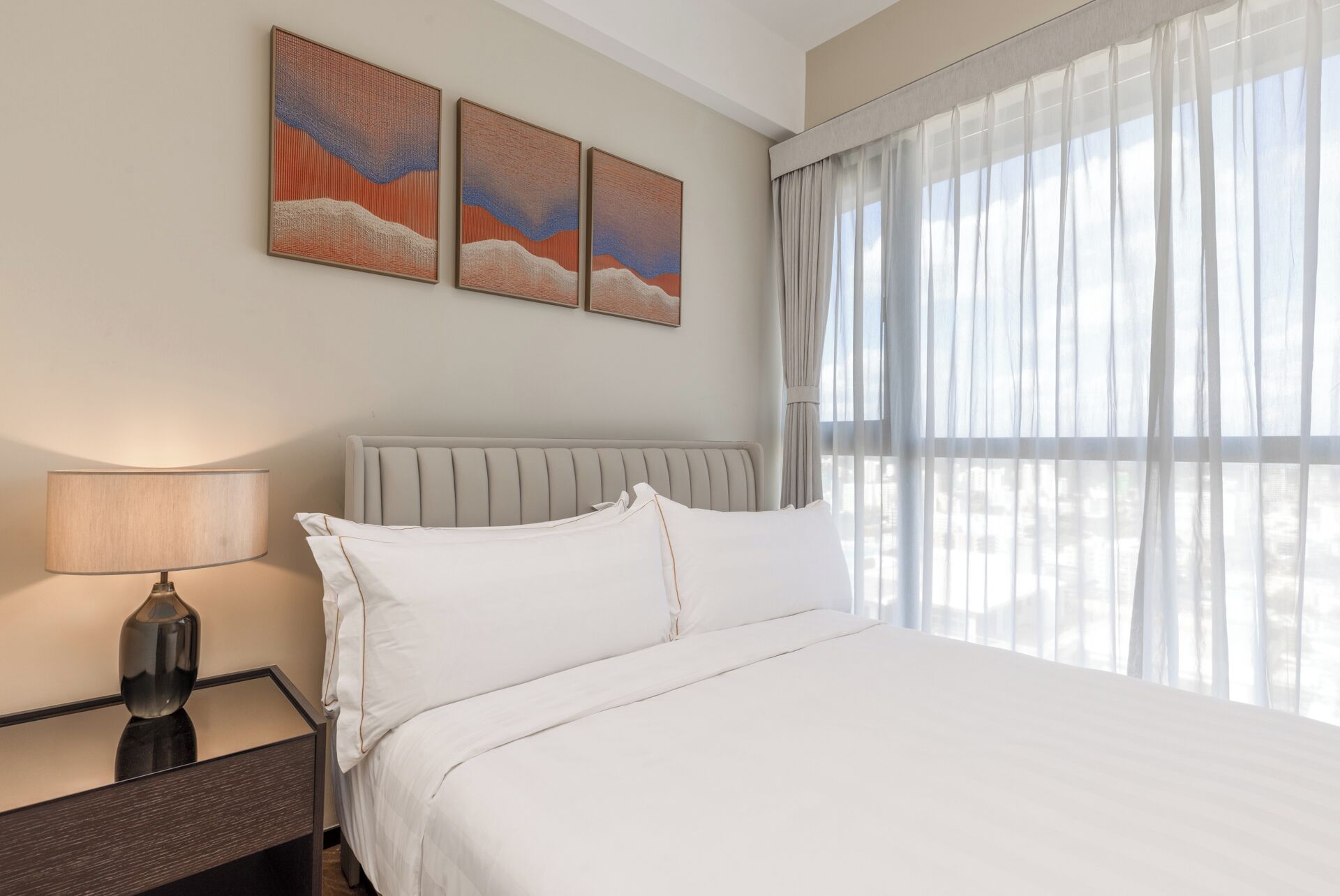 A hotel room with a bed, a nightstand, a lamp, and three paintings on the wall.