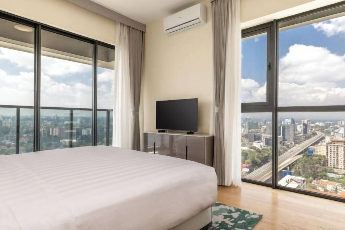 Une chambre d’hôtel située dans un immeuble de grande hauteur, dotée d’un grand lit, d’un téléviseur à écran plat et offrant une vue sur la ville grâce à de grandes fenêtres du sol au plafond.