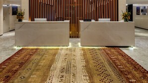 Zona de recepción con diseño moderno, que presenta una estructura central de paneles de madera, una alfombra estampada y un aplique de techo decorativo.