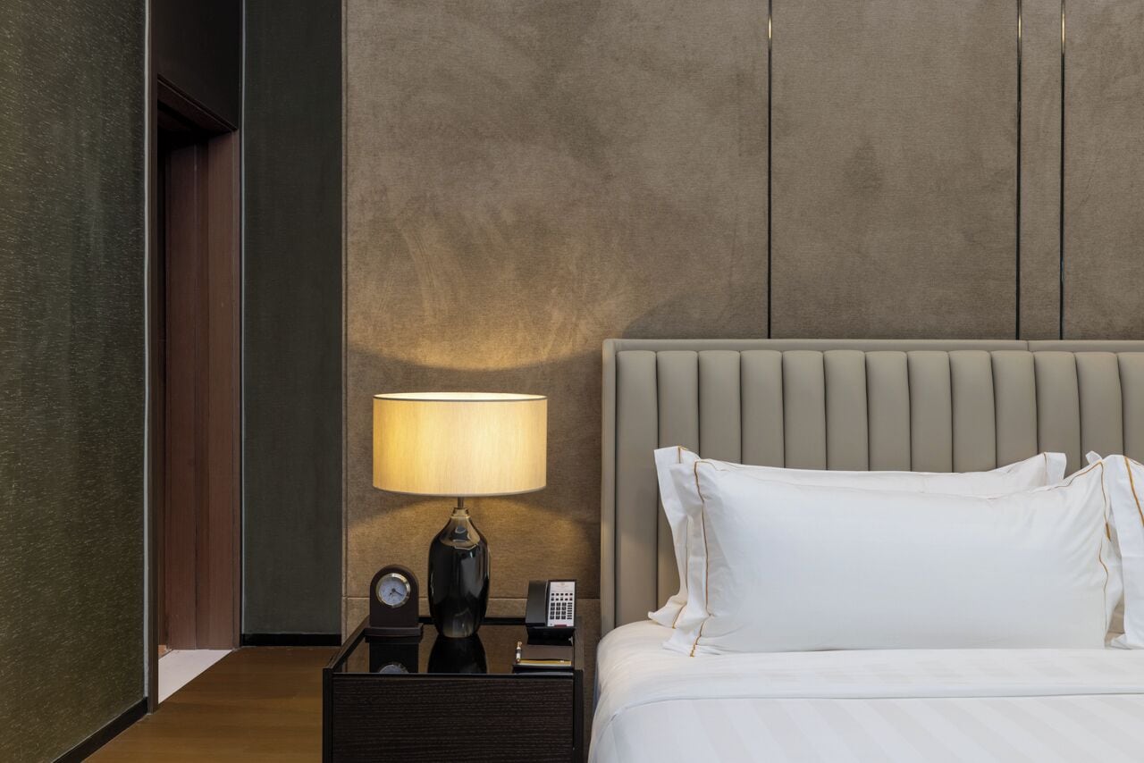 A hotel room with a bed, a nightstand with a lamp, a clock, and a telephone.