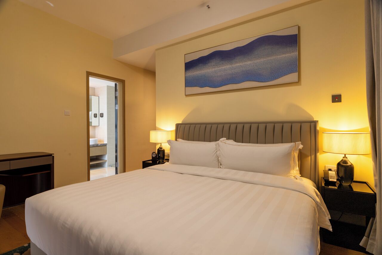 A hotel room with a large bed, two bedside tables with lamps, a headboard, and a painting on the wall.