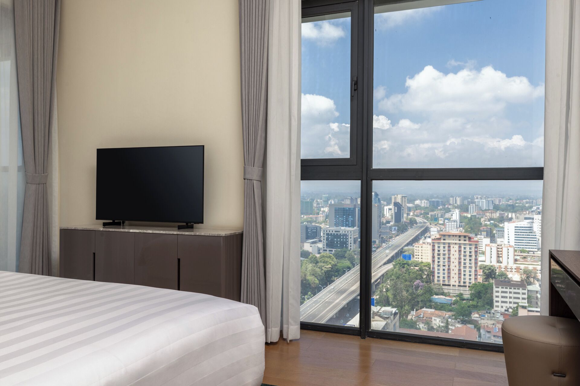 A hotel room with a large window, a bed, a flat-screen TV, and a desk.