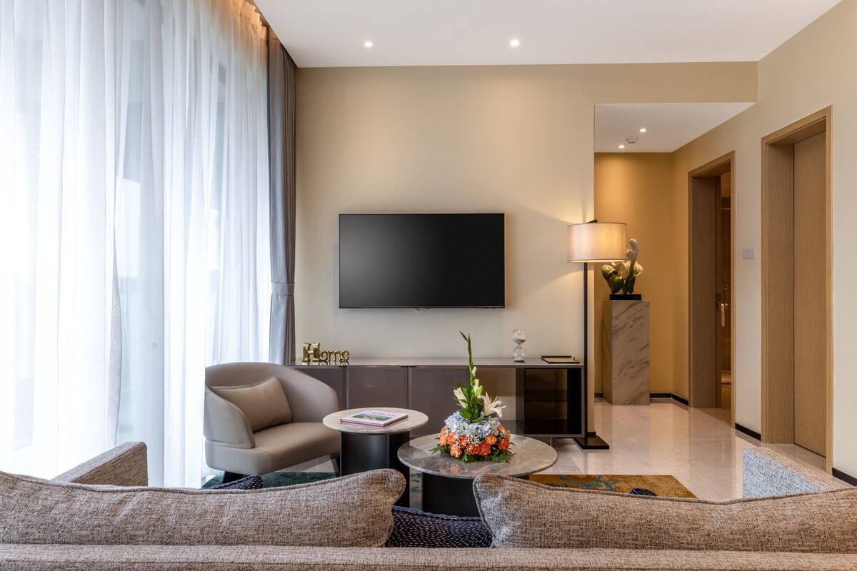 Un salon moderne avec un canapé, une table basse, un téléviseur fixé au mur et une lampe.